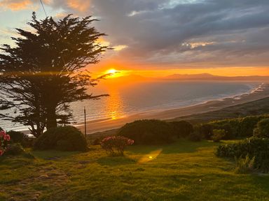 A sunset over an ocean with a sandy beach trees bushes and grass in the foreground at Sibrwd Y Mor in Harlech