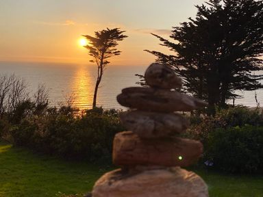A sunset over the ocean with trees and a stack of rocks in the foreground at Sibrwd Y Mor in Harlech