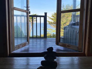 A wooden deck with railing and trees beyond overlooking a body of water seen through open glass doors at Sibrwd Y Mor in Harlech