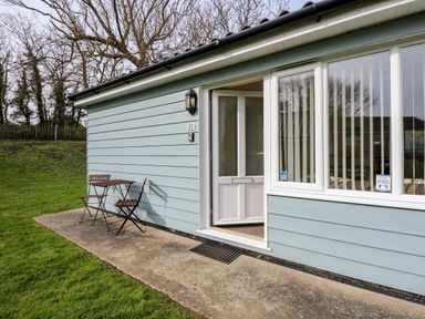 Exterior view of a light blue building with a half-open door and a small wooden table with two chairs on a concrete patio at 11 The Dell in Mundesley