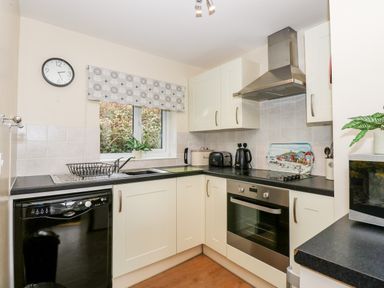 A kitchen with white cabinets a dishwasher oven microwave and a window with a decorative blind at 11 The Dell in Mundesley