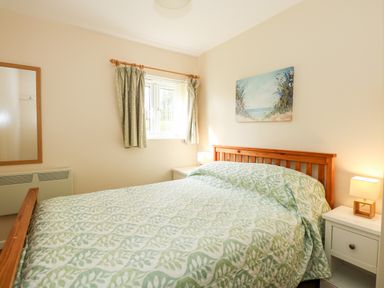 A bedroom with a wooden framed bed and patterned bedspread next to bedside tables with lamps and a window with curtains at 11 The Dell in Mundesley