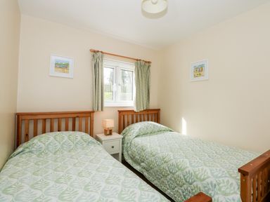 A bedroom with two single beds green patterned bedding a window and a small bedside table with a lamp at 11 The Dell in Mundesley