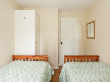 A bedroom with two single beds a white wardrobe a door and a wall mirror at 11 The Dell in Mundesley