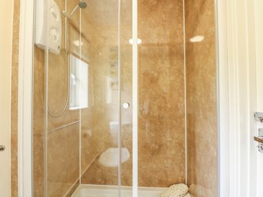 A shower enclosure with beige marble walls and a handheld showerhead at 11 The Dell in Mundesley