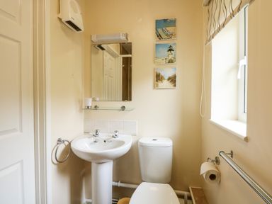 A bathroom with a pedestal sink a toilet a mirror and a window at 11 The Dell in Mundesley