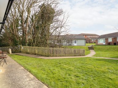 A grassy outdoor area with paved paths and fenced trees near residential buildings at 11 The Dell in Mundesley