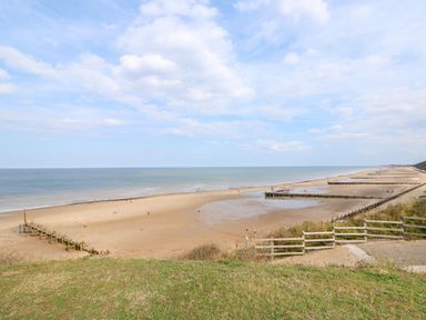 A sandy beach with wooden groynes and a grassy area in the foreground at 11 The Dell in Mundesley