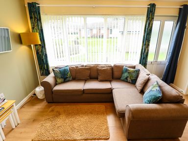 A living room with a brown corner sofa and a yellow floor lamp at 11 The Dell in Mundesley