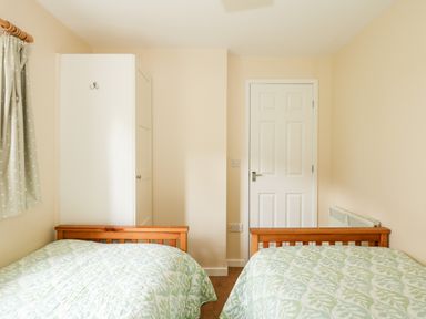 A bedroom with two beds wooden frames a white wardrobe a white door and green patterned curtains at 12 The Dell in Mundesley