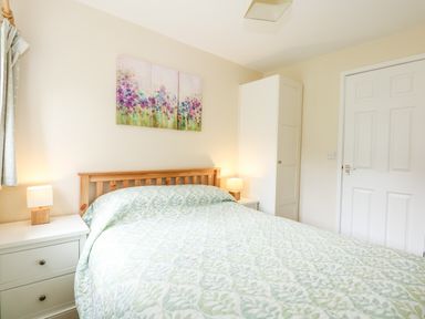 A bedroom with a bed a wooden headboard bedside tables lamps a white wardrobe and floral artwork above the bed at 12 The Dell in Mundesley