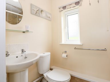 A bathroom with a pedestal sink toilet paper holder towel rail and a window at 12 The Dell in Mundesley