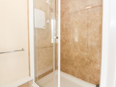 A shower enclosure with glass door beige tiled walls and a wall-mounted shower unit with controls at 12 The Dell in Mundesley