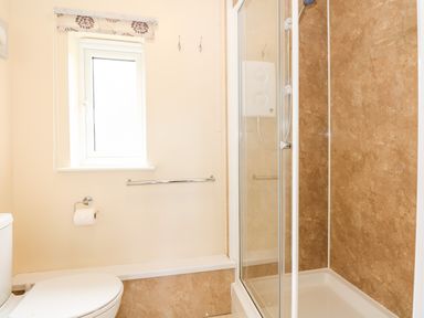 A bathroom with a toilet a window a toilet paper holder a towel rail and a shower enclosure at 12 The Dell in Mundesley