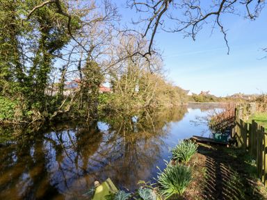 A river with trees on one side and a fenced grassy bank with plants on the other at 12 The Dell in Mundesley