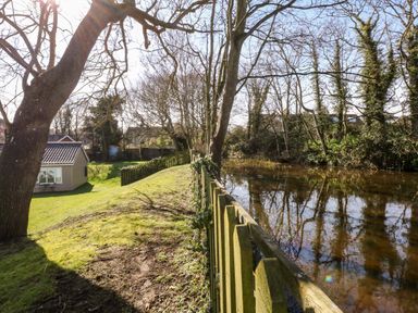 A garden with fenced river trees and a small shed at 12 The Dell in Mundesley