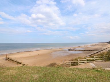 A sandy beach with wooden groynes and people walking at 12 The Dell in Mundesley