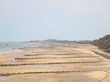 A sandy beach with groynes extending into the sea and a town in the distance at 12 The Dell in Mundesley