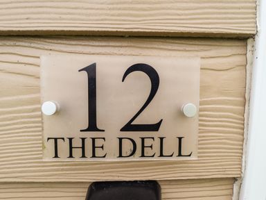 A house number sign with 12 and the name The Dell on a beige textured wall at 12 The Dell in Mundesley