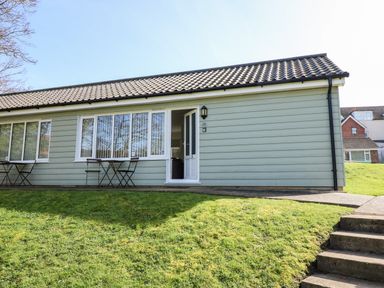 Exterior view of a single-story building with green siding small tables and chairs outside at 14 The Dell in Mundesley
