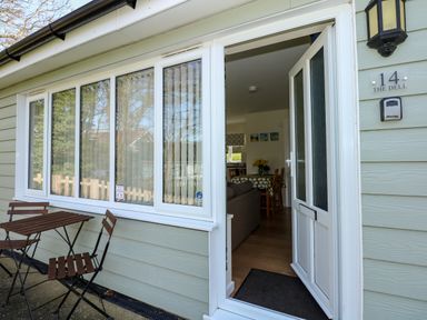 A small outdoor patio with a table and two chairs and a partially open door leading into a dining area at 14 The Dell in Mundesley