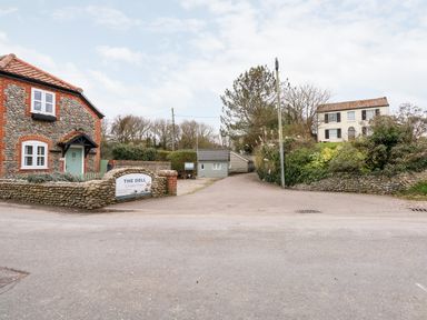 A road entrance to The Dell Chalet Park with stone and brick houses and vegetation at Mundesley
