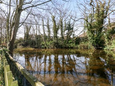 A fenced pond with trees around it and houses visible in the background at 15 The Dell in Mundesley