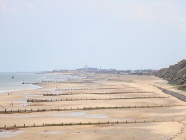 A sandy beach with wooden groynes extending into the sea and cliffs on the right at 15 The Dell in Mundesley