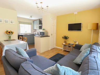 A living room with a sofa and dining area at 15 The Dell Mundesley