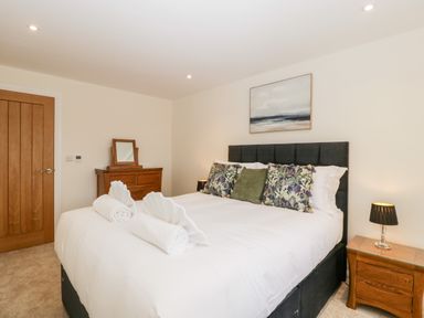 A bedroom with a large bed with white linens and decorative pillows a wooden door a wooden dresser with a mirror and a wooden nightstand with a lamp above the bed hangs a landscape painting at Bilsham Meadows in Aust