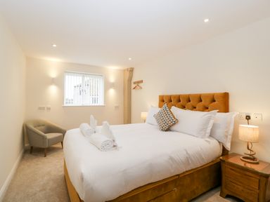 A bedroom with a large bed a bedside table with a lamp a grey chair and a window at Bilsham Meadows in Aust