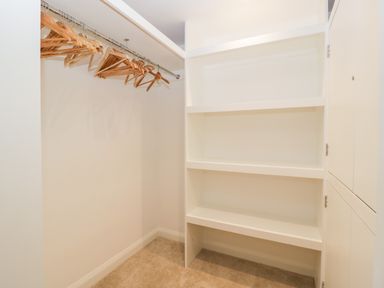 A walk-in closet with wooden hangers on a metal rod and built-in white shelves at Bilsham Meadows in Aust