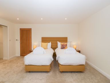 A bedroom with two single beds with white bedding and pillows and a wooden door at Bilsham Meadows in Aust