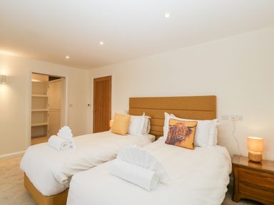 A bedroom with two single beds white linens folded towels bedside table with lamp and wooden doors at Bilsham Meadows in Aust