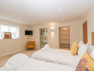 A bedroom with two beds yellow pillows an orange chair a wall mounted tv and an open door revealing shelves at Bilsham Meadows in Aust