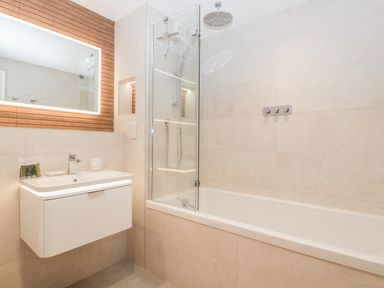 A bathroom with a white bathtub and shower area next to a white sink and a backlit mirror at Bilsham Meadows in Aust