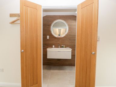 A bathroom with wooden double doors a wall-mounted sink and round mirror at Bilsham Meadows in Aust