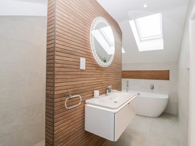 A bathroom with a white floating sink, a round mirror on a wooden wall, and a white bathtub under skylights at Bilsham Meadows in Aust