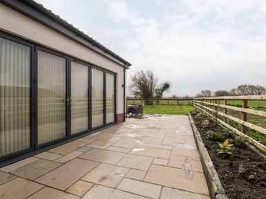 A patio with stone tiles next to a house with large glass doors and a garden with a wooden fence at Bilsham Meadows in Aust