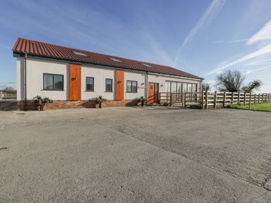 A single story building with tiled roof wooden door and windows next to a fence and open area at Bilsham Meadows in Aust