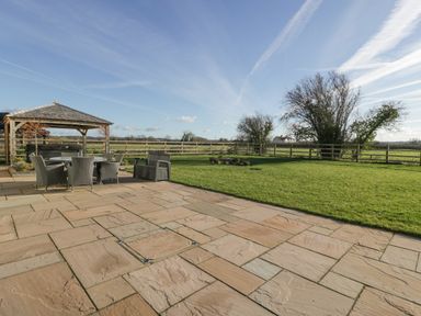 An outdoor patio with tiled flooring a round table with chairs and a wooden gazebo next to a grassy field at Bilsham Meadows in Aust