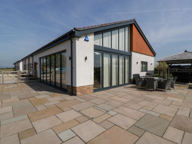 The exterior of a modern building with large glass doors and windows a patio with outdoor table and chairs at Bilsham Meadows in Aust