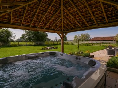 An outdoor hot tub under a wooden pergola with a lawn garden and patio furniture at Bilsham Meadows in Aust