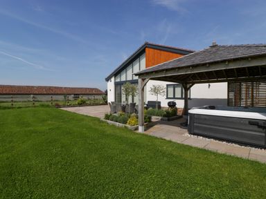 A garden with a patio table and chairs a hot tub under a wooden gazebo and a modern house at Bilsham Meadows in Aust