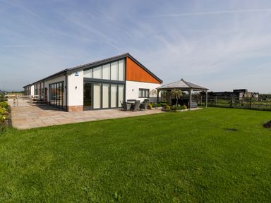 A modern house with a patio and outdoor furniture next to a gazebo on a grass lawn at Bilsham Meadows in Aust