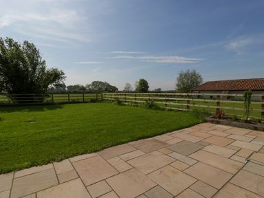 A patio with stone tiles next to a fenced grassy yard with trees and a building in the background at Bilsham Meadows in Aust