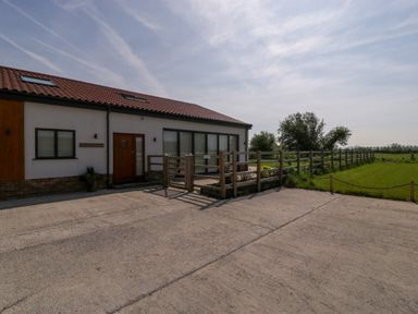 A building with a tiled roof and wooden door next to a wooden fence and green grass at Bilsham Meadows in Aust