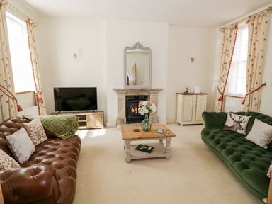 A living room with two sofas a wooden coffee table a fireplace a television and floral curtains at 4 The Old Council House Shipston-On-Stour