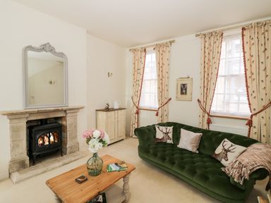 A living room with a green sofa, wooden coffee table, stone fireplace, and floral curtains at 4 The Old Council House in Shipston-On-Stour