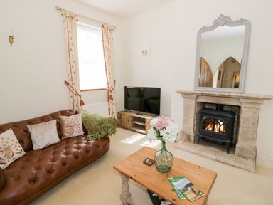 A living room with a brown leather sofa cushions a green throw a wooden coffee table with flowers magazines a stone fireplace with a mirror and a television at 4 The Old Council House Shipston-On-Stour